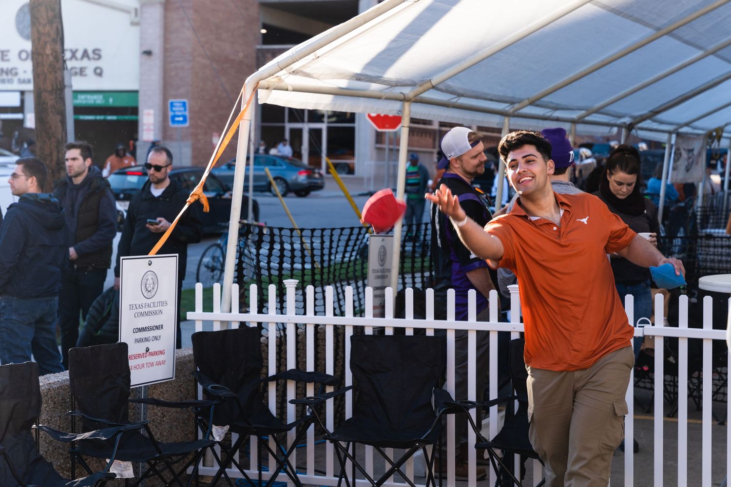 Person in orange shirt playing games at an outdoor event with white picket fence barrier.