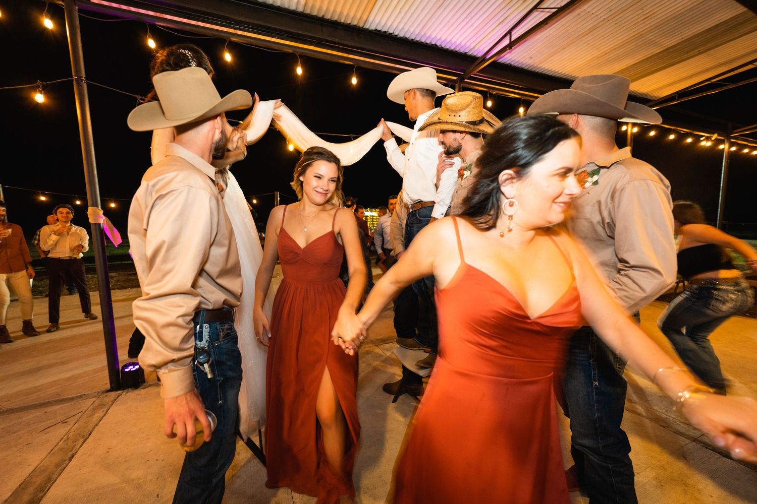 Couples dance together at a rustic reception venue with string lights overhead.