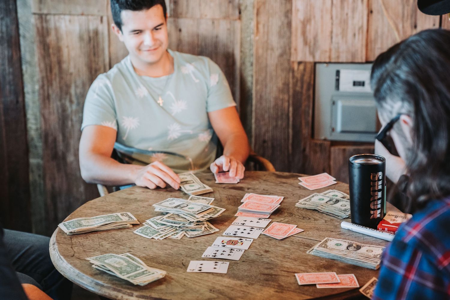 A card game in progress on a rustic wooden table with cash and playing cards scattered across the surface.
