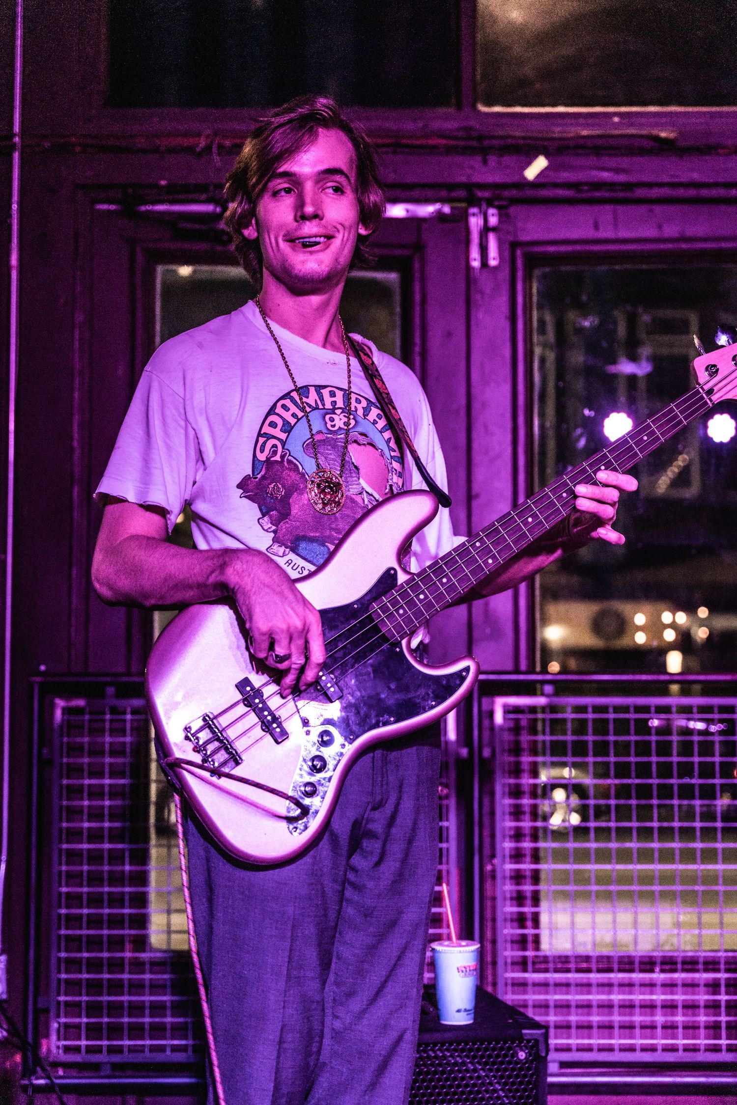 Bassist performs on stage in purple lighting while playing electric bass guitar and wearing a vintage t-shirt.