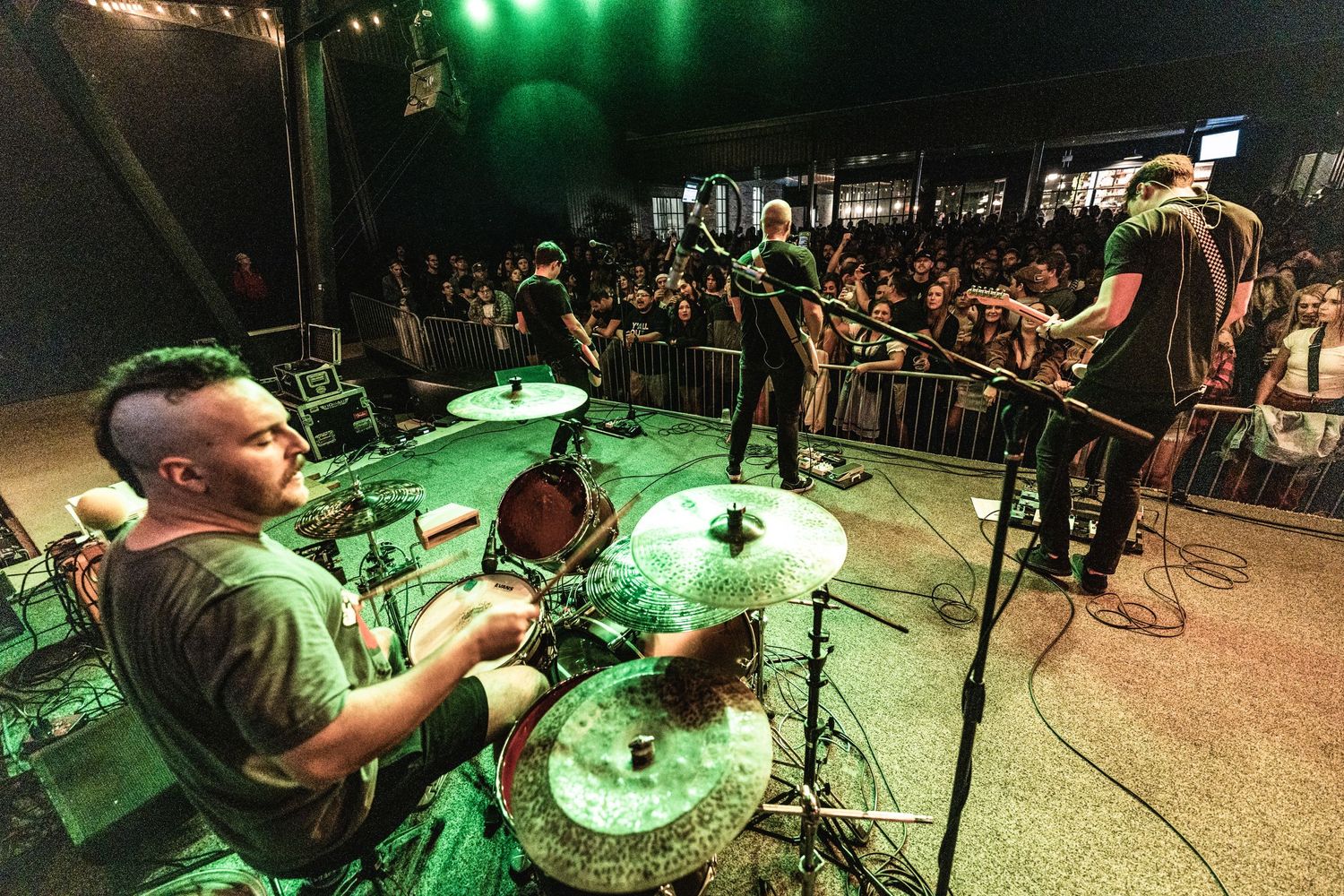 Wide angle shot of rock band performing on stage with dramatic lighting and enthusiastic crowd.