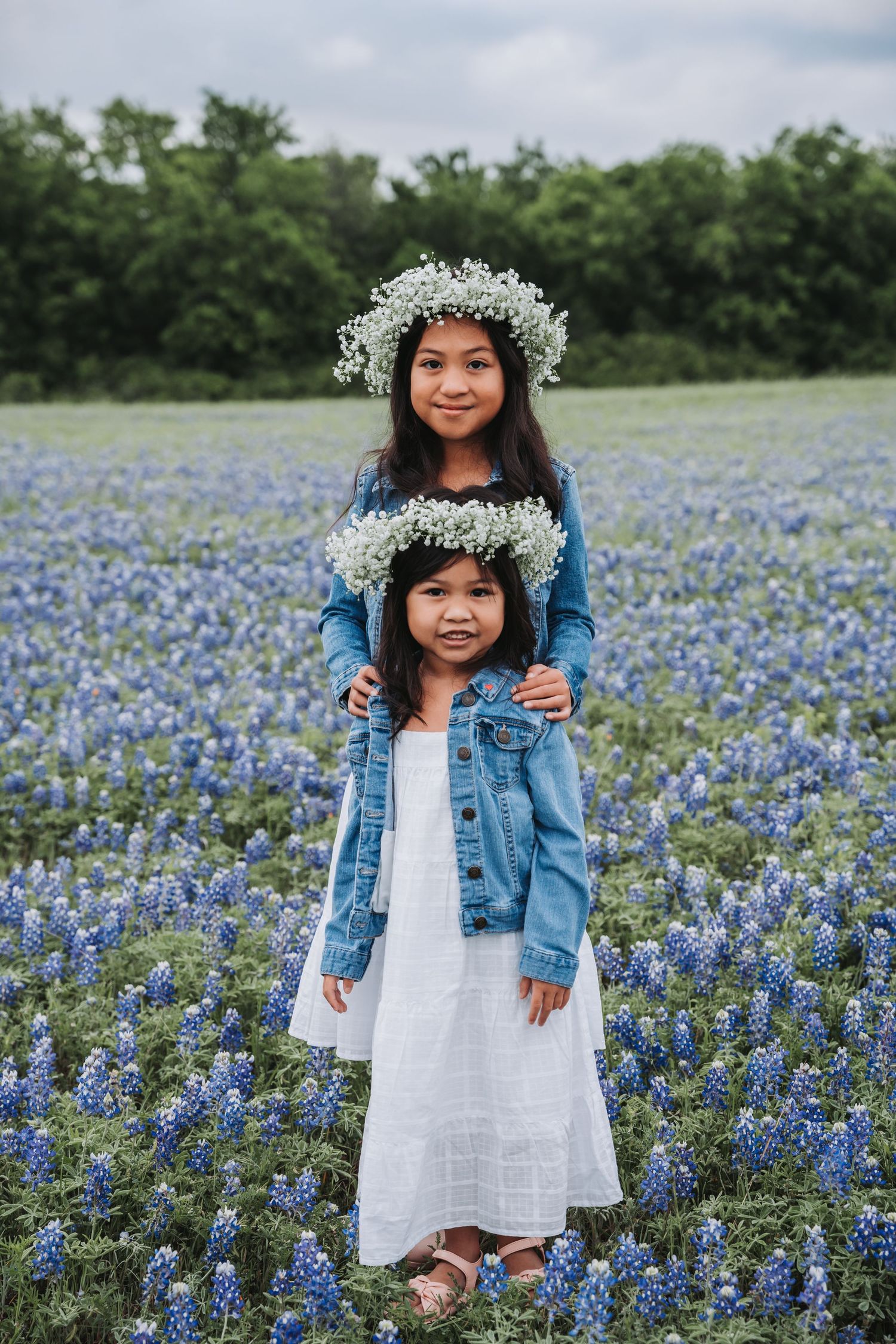 Two figures wearing white baby's breath crowns stand in a field of bluebonnets.