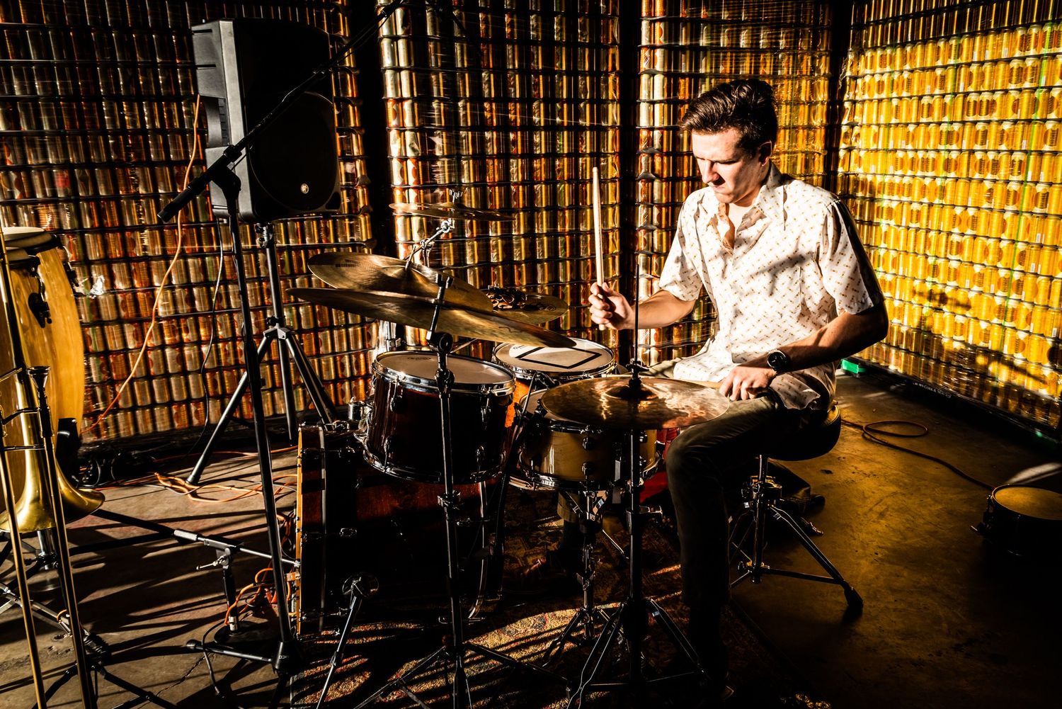 Drummer performs on stage with dramatic lighting against textured gold wall.