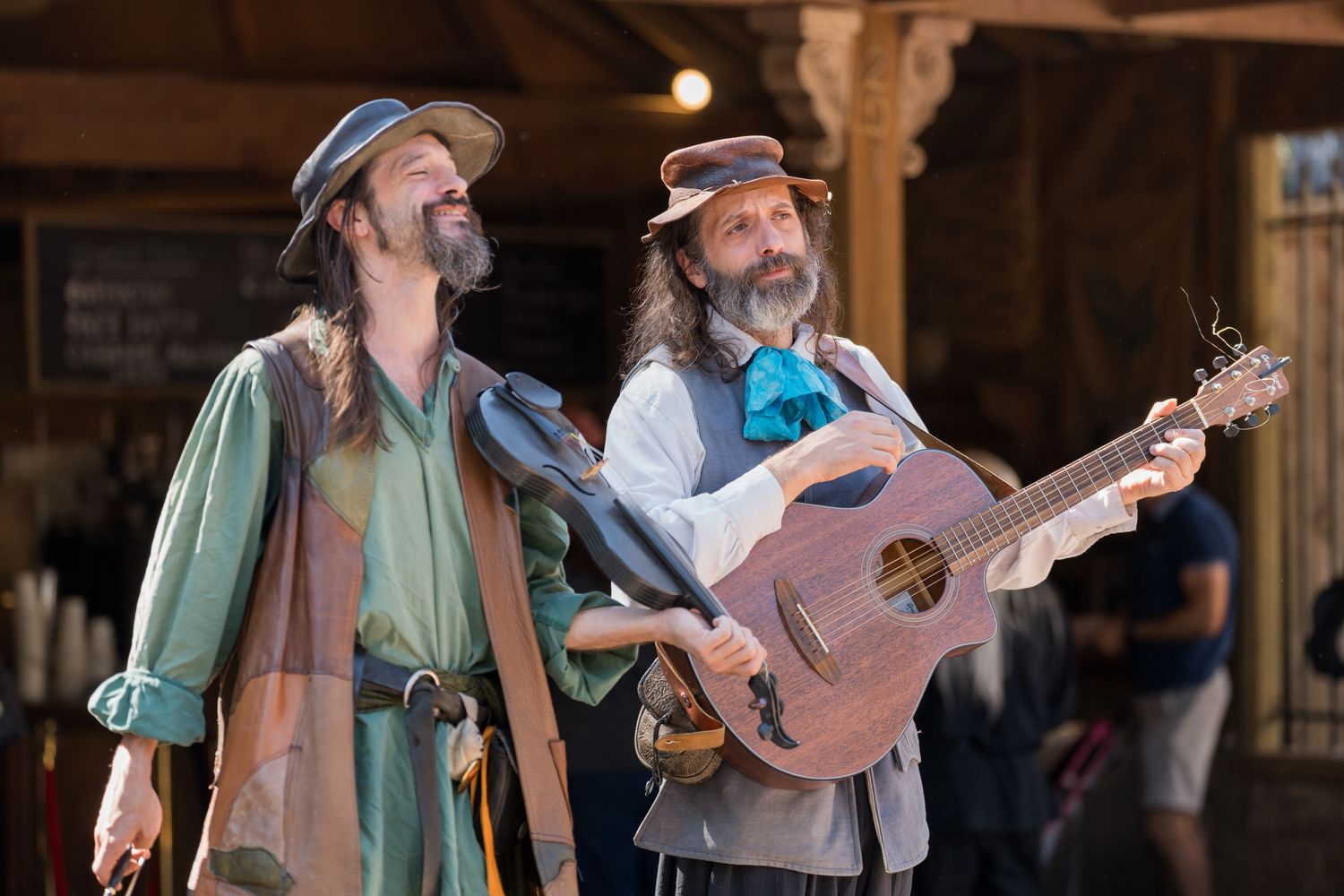 Two performers in renaissance garb sing and play guitar together during an outdoor festival performance.