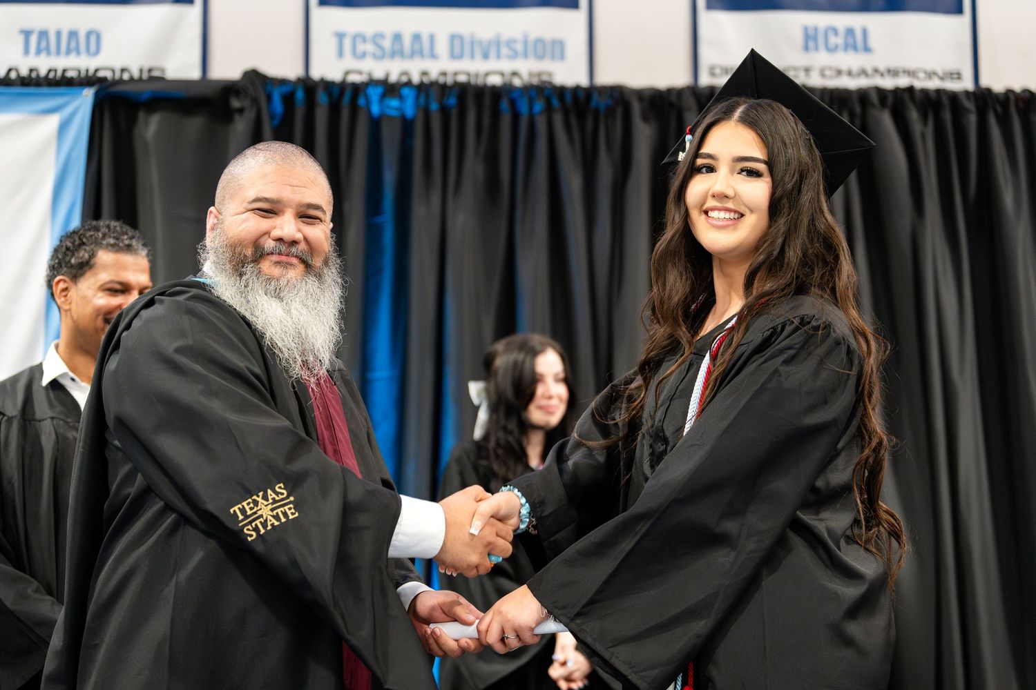 Graduate receives diploma and congratulatory handshake during graduation ceremony.