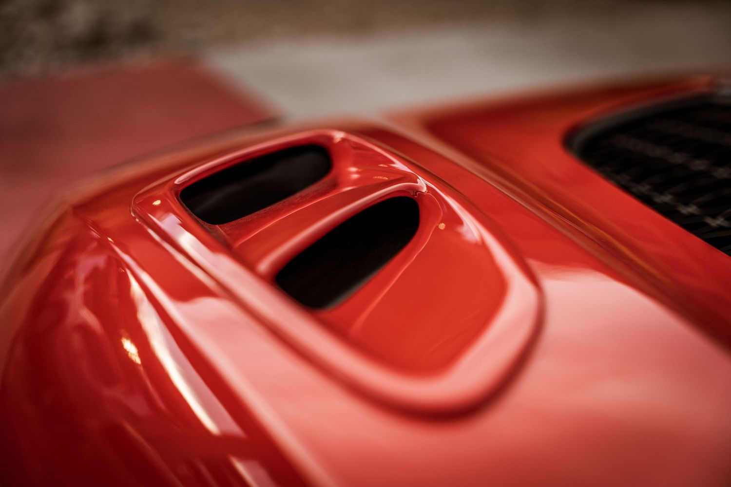 Red hood scoop detail on a sports car showing curved air intake vents.