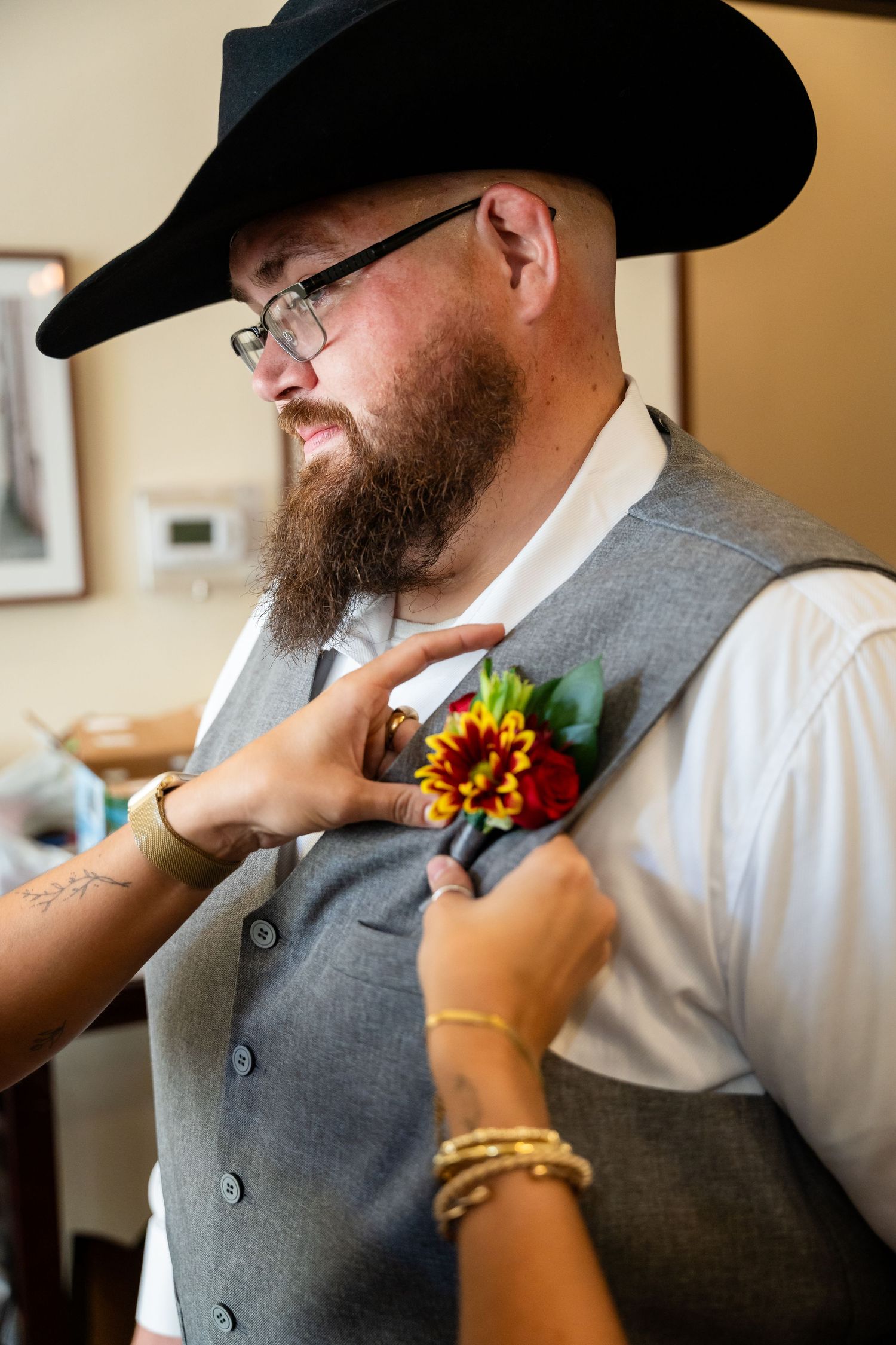 Boutonniere with orange and red flowers being pinned to a grey vest.