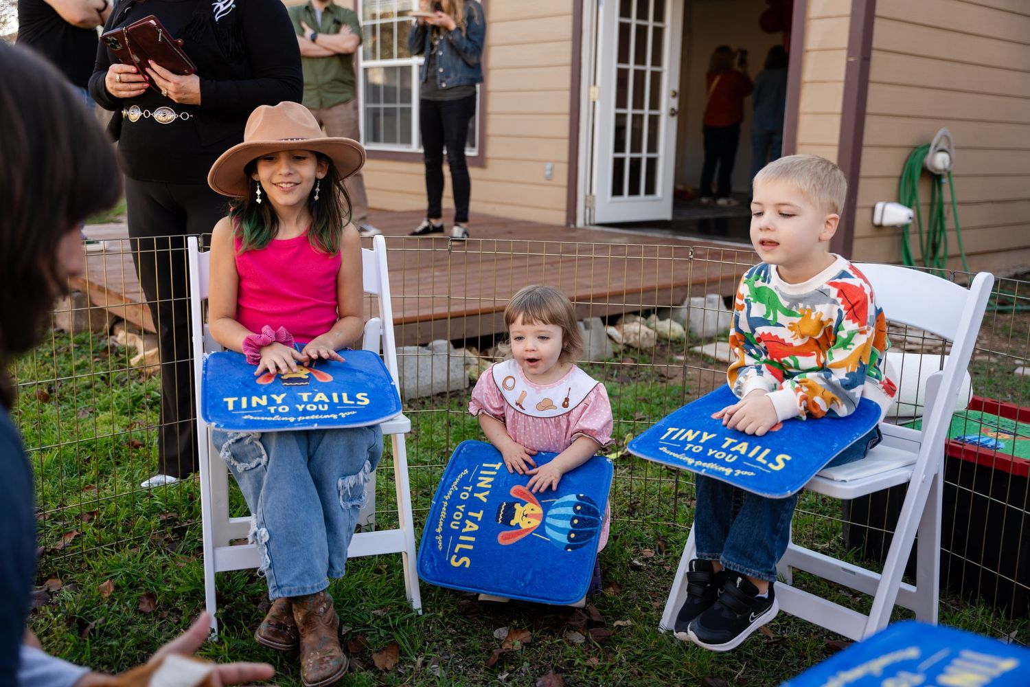 People enjoying an outdoor party with pizza gathered on white chairs in a backyard garden setting.