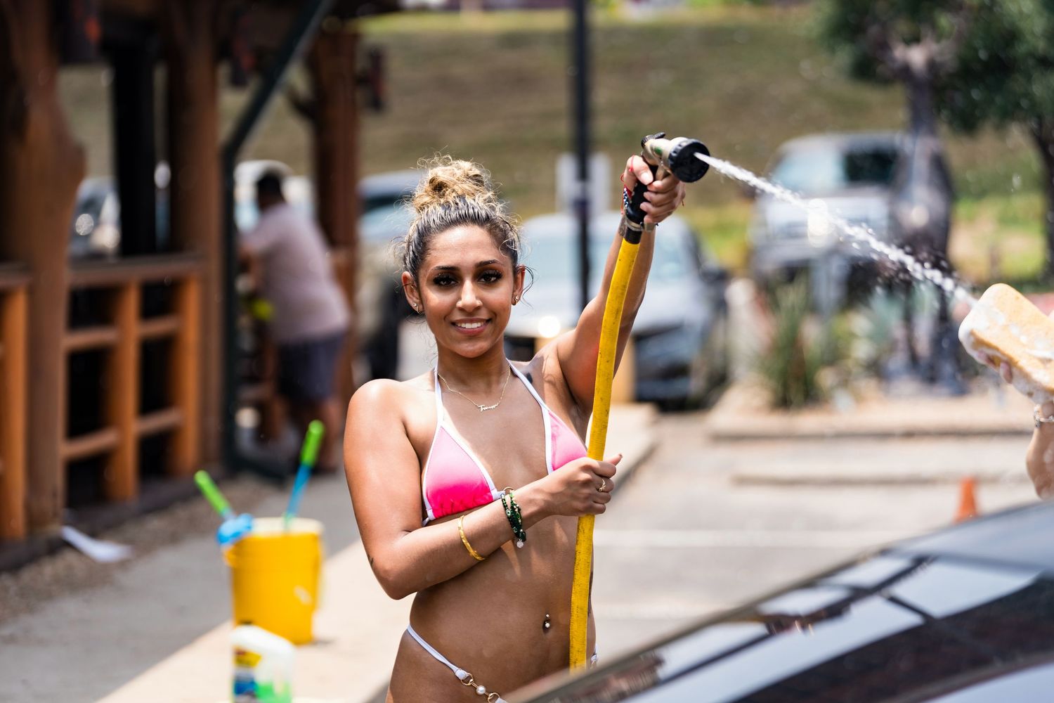 Person in pink swimwear spraying water during outdoor car wash.