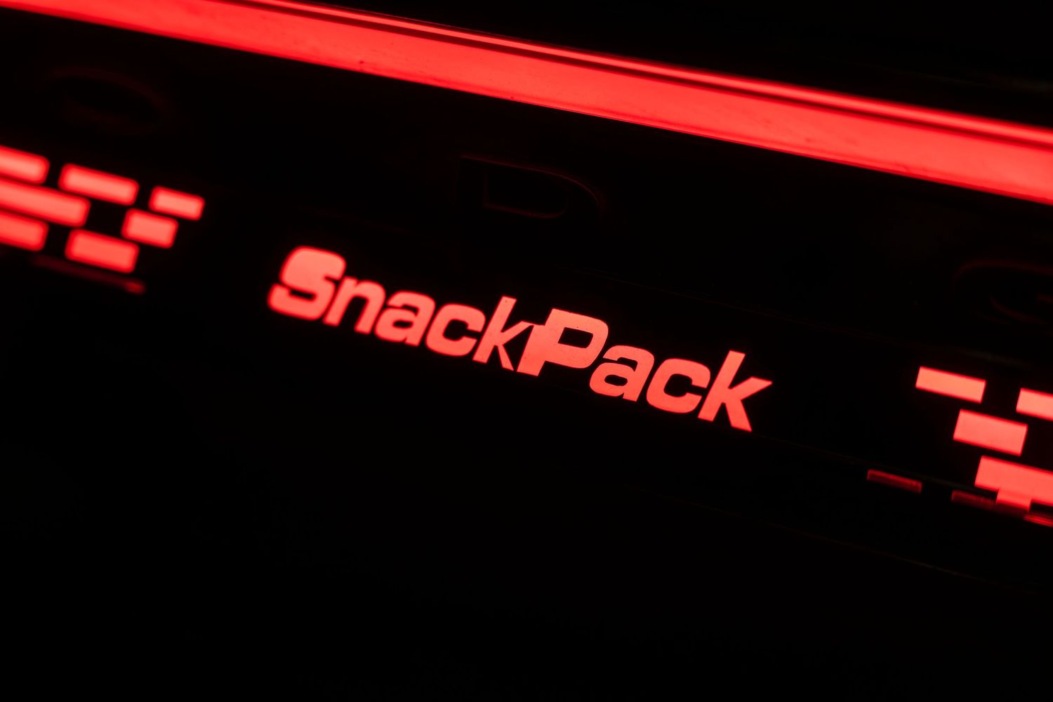 Close-up of red neon SnackPack text signage in dark environment.