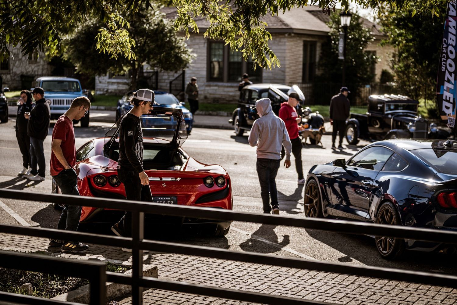 Group gathering around exotic sports cars displayed on a brick paved street.