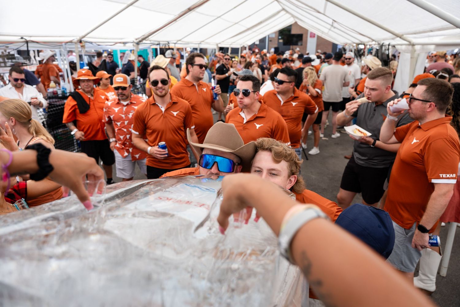 Large crowd in orange shirts gathers under a white tent at a vibrant outdoor festival.