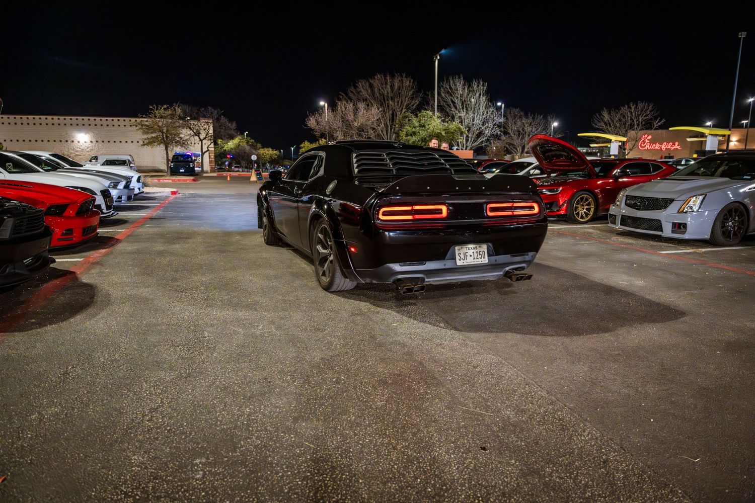 Black Dodge Challenger parked in nighttime parking lot.