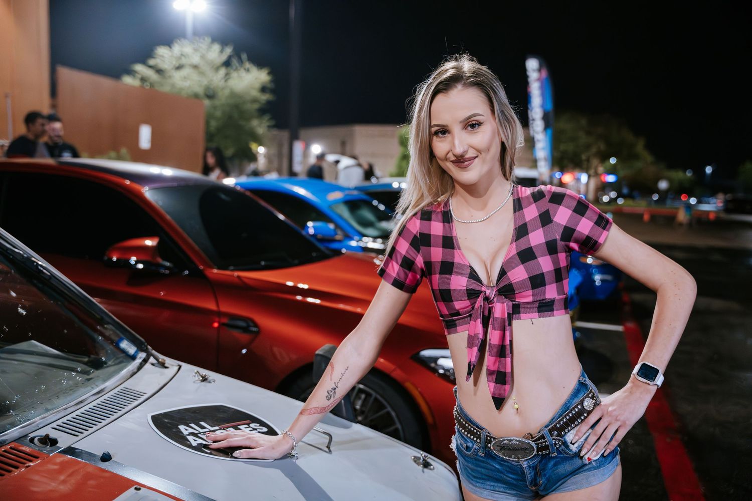 Pink checkered tied top with denim shorts posing by modified cars.