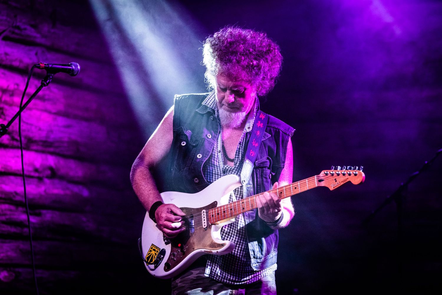 Guitar player performs on stage bathed in dramatic purple concert lighting.