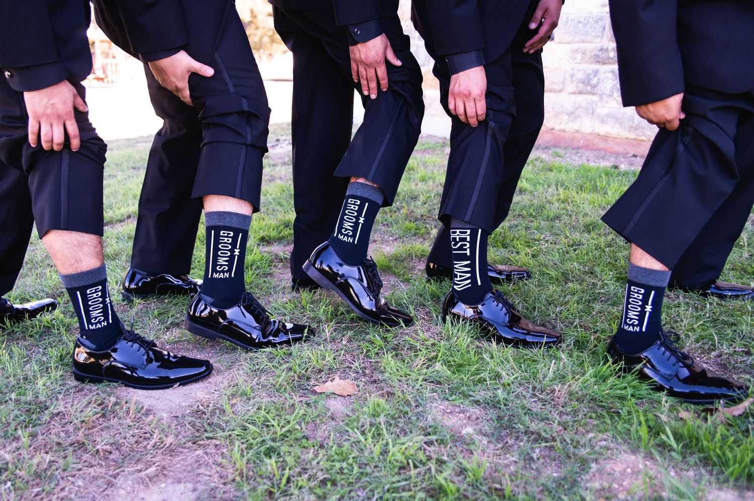 Wedding party shows off matching Navy blue socks and dress shoes while standing on grass.