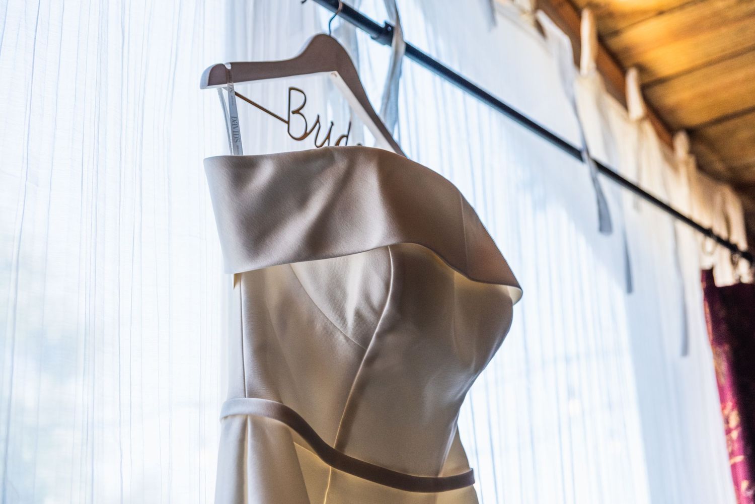 A white wedding dress hangs elegantly against a rustic wooden wall.