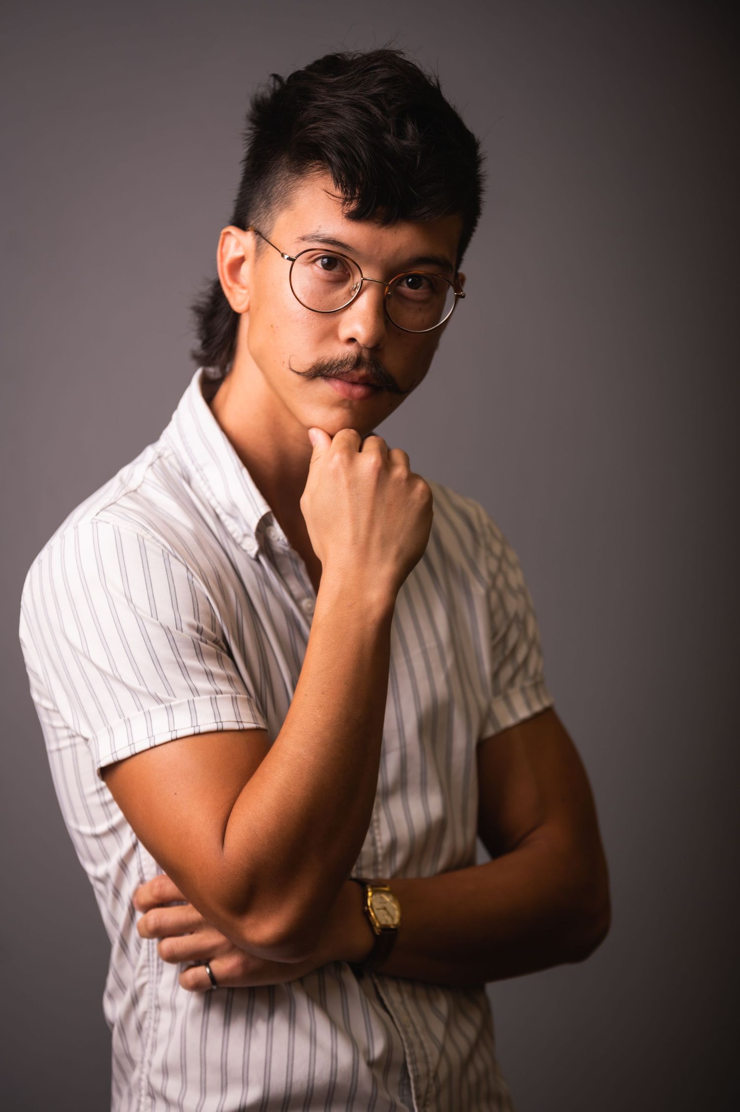 Thoughtful portrait against grey background wearing striped shirt and glasses.