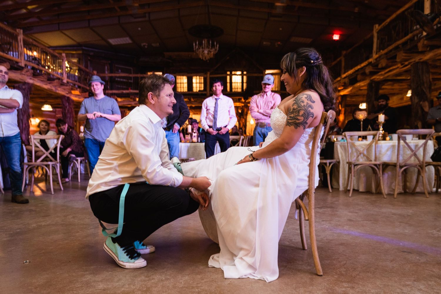 A traditional garter removal moment during a wedding reception in a rustic barn setting.