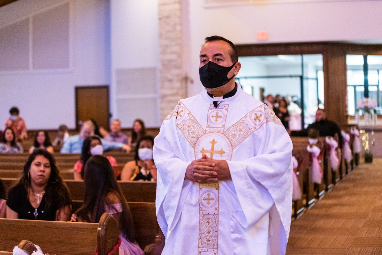 Priest in white robes and black mask leads Catholic wedding ceremony.
