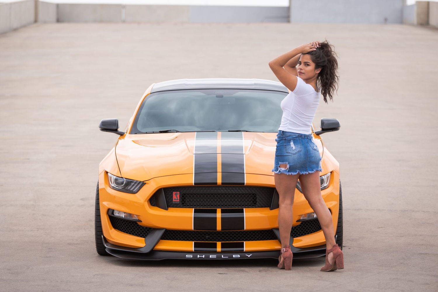 Orange Ford Mustang with black racing stripes parked in a concrete outdoor setting.