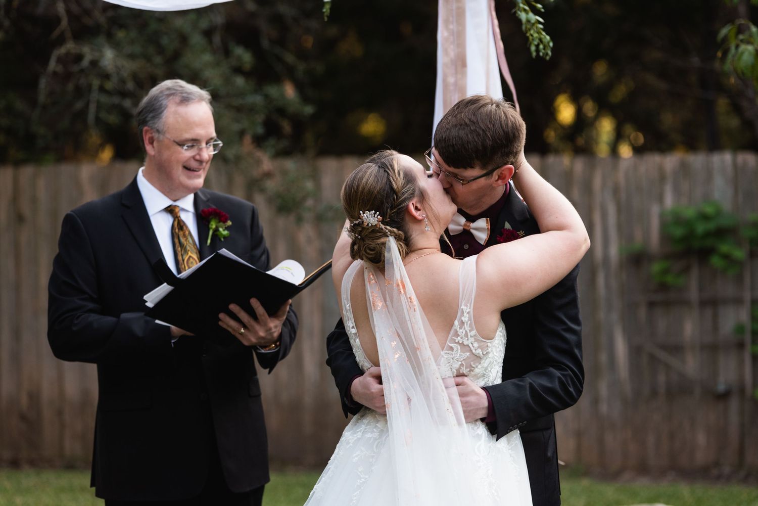 A newlywed couple shares their first kiss during an outdoor garden wedding ceremony.