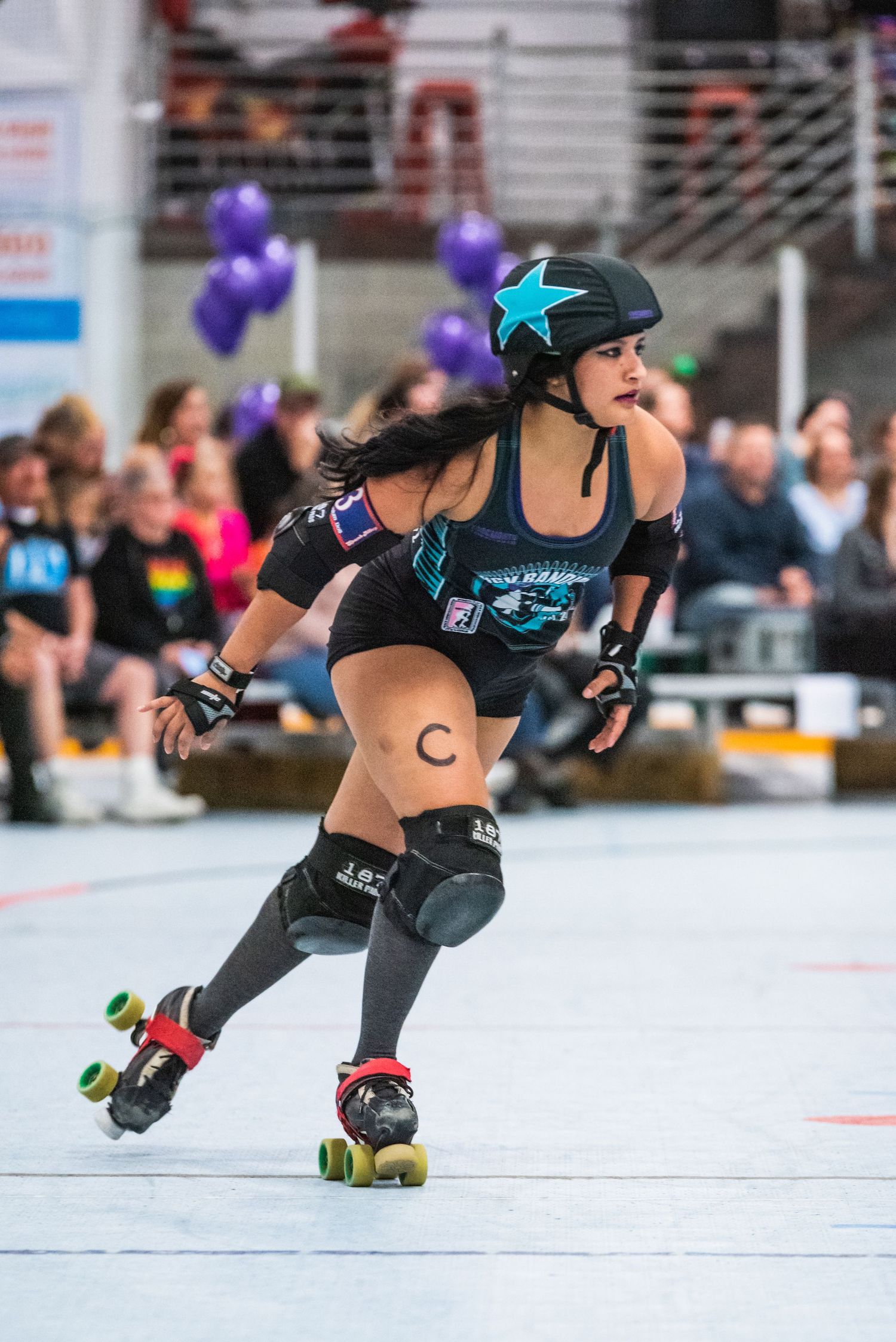 Roller derby skater in black and blue uniform speeds around rink with determined stance.