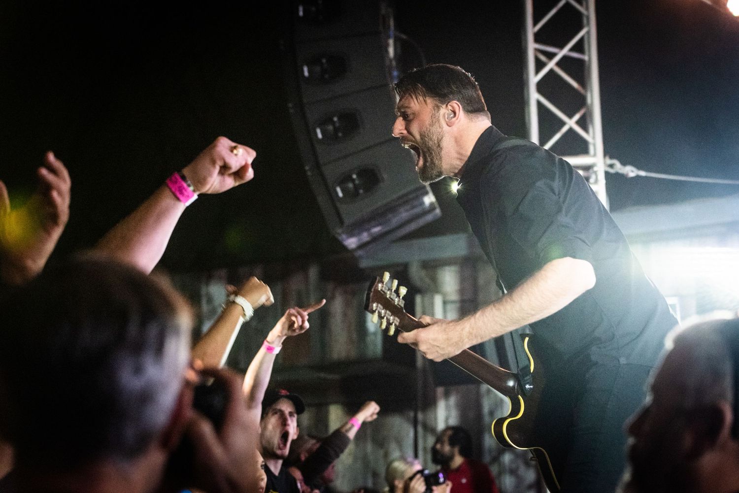 Musician energetically performs above reaching crowd during intense concert moment.