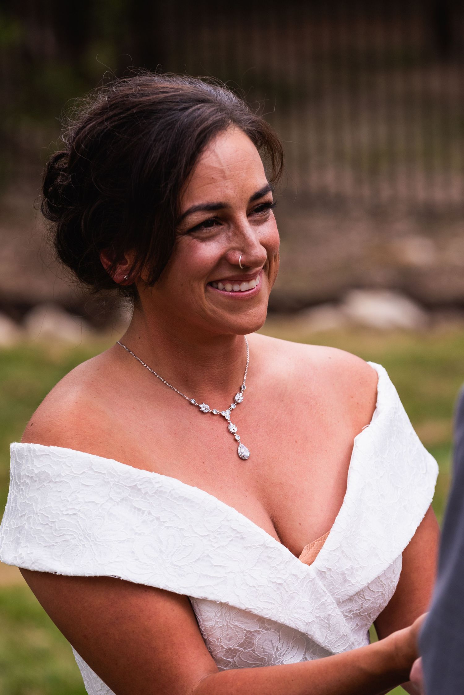 Radiant bride wearing off-shoulder gown and crystal necklace smiles joyfully.