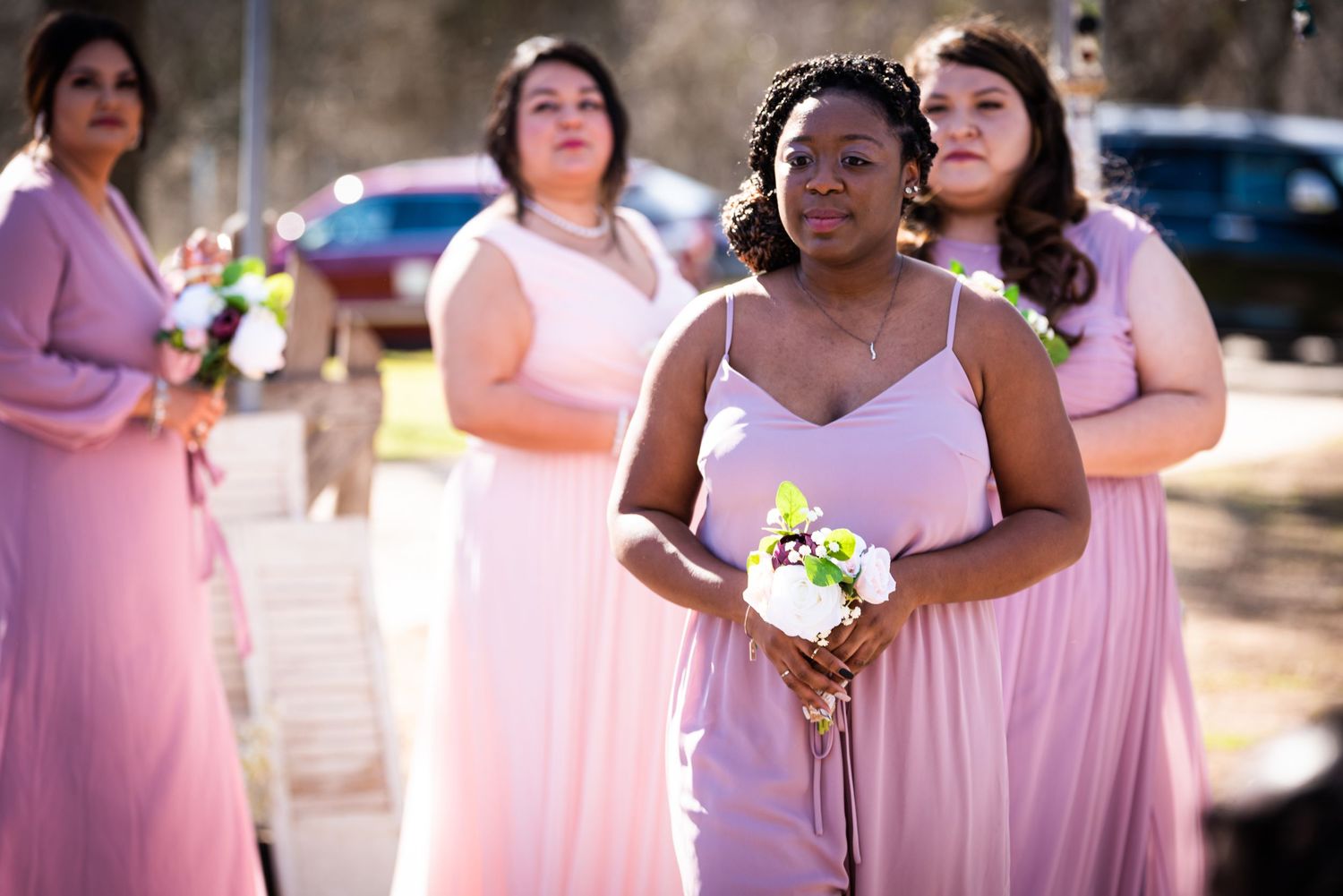 Bridesmaids in pink dresses holding bouquets during outdoor wedding ceremony.