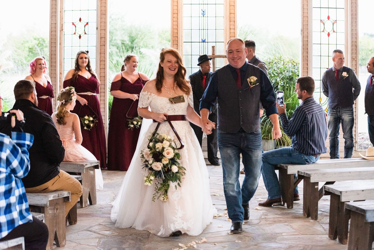 Wedding ceremony attendees gather inside a rustic chapel with wooden benches.