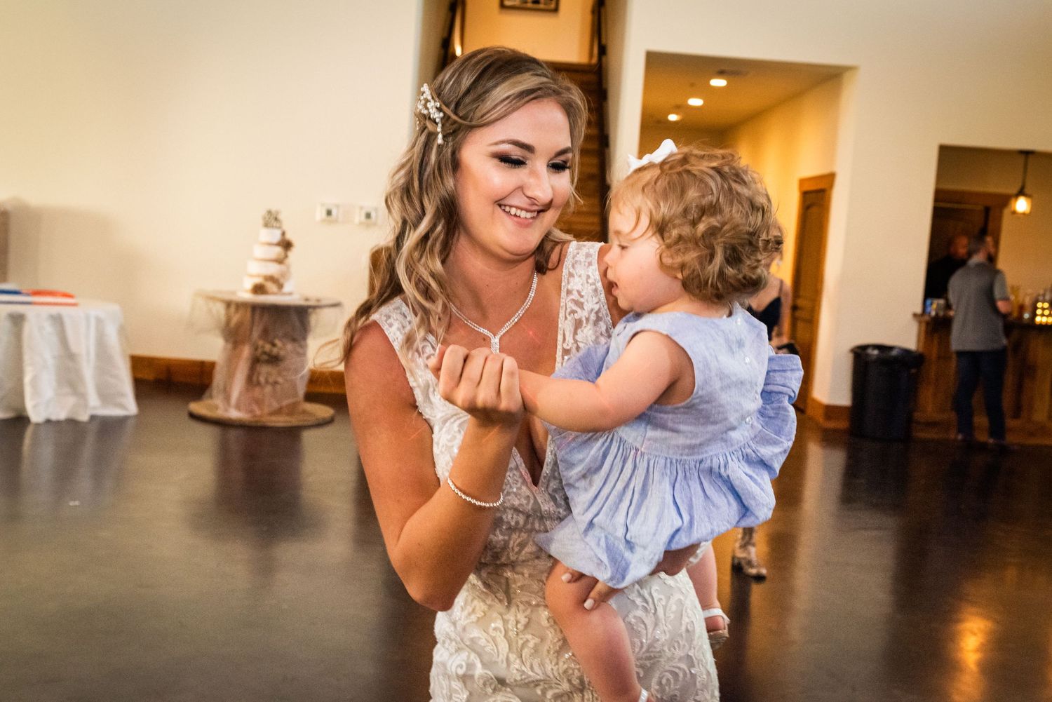 A tender moment shared between a woman in a formal gown and a small child in a light blue dress at a wedding reception.