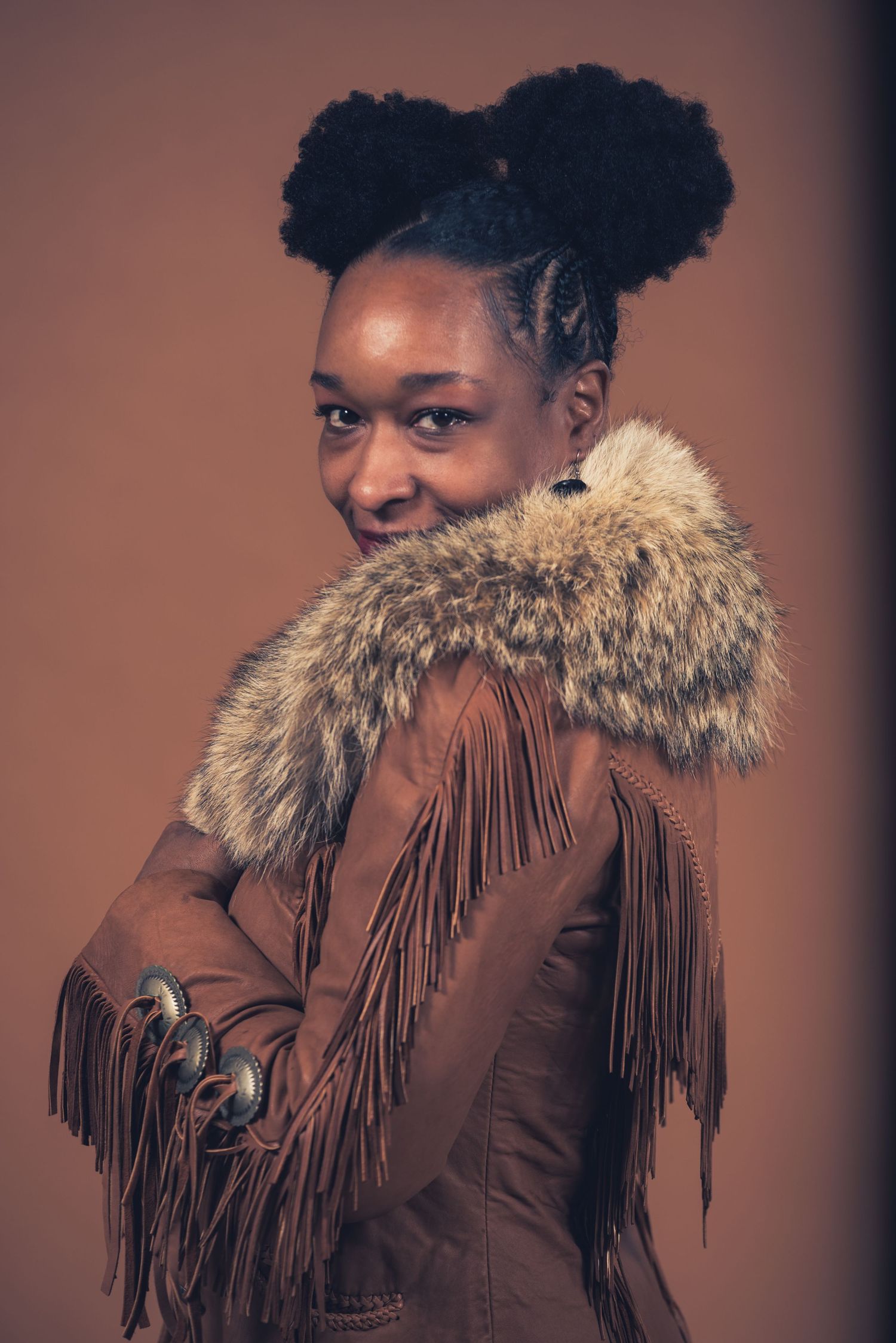 Portrait in brown fringe jacket with fur collar showing confident pose.