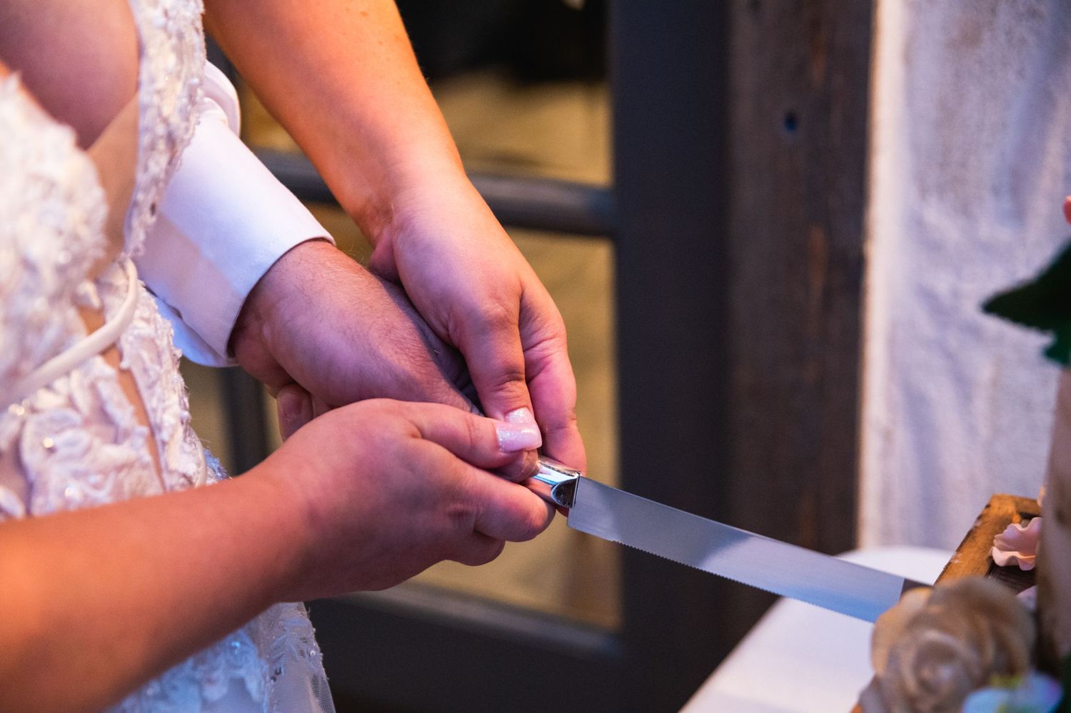 Close-up shot of hands cutting a wedding cake with a silver knife.