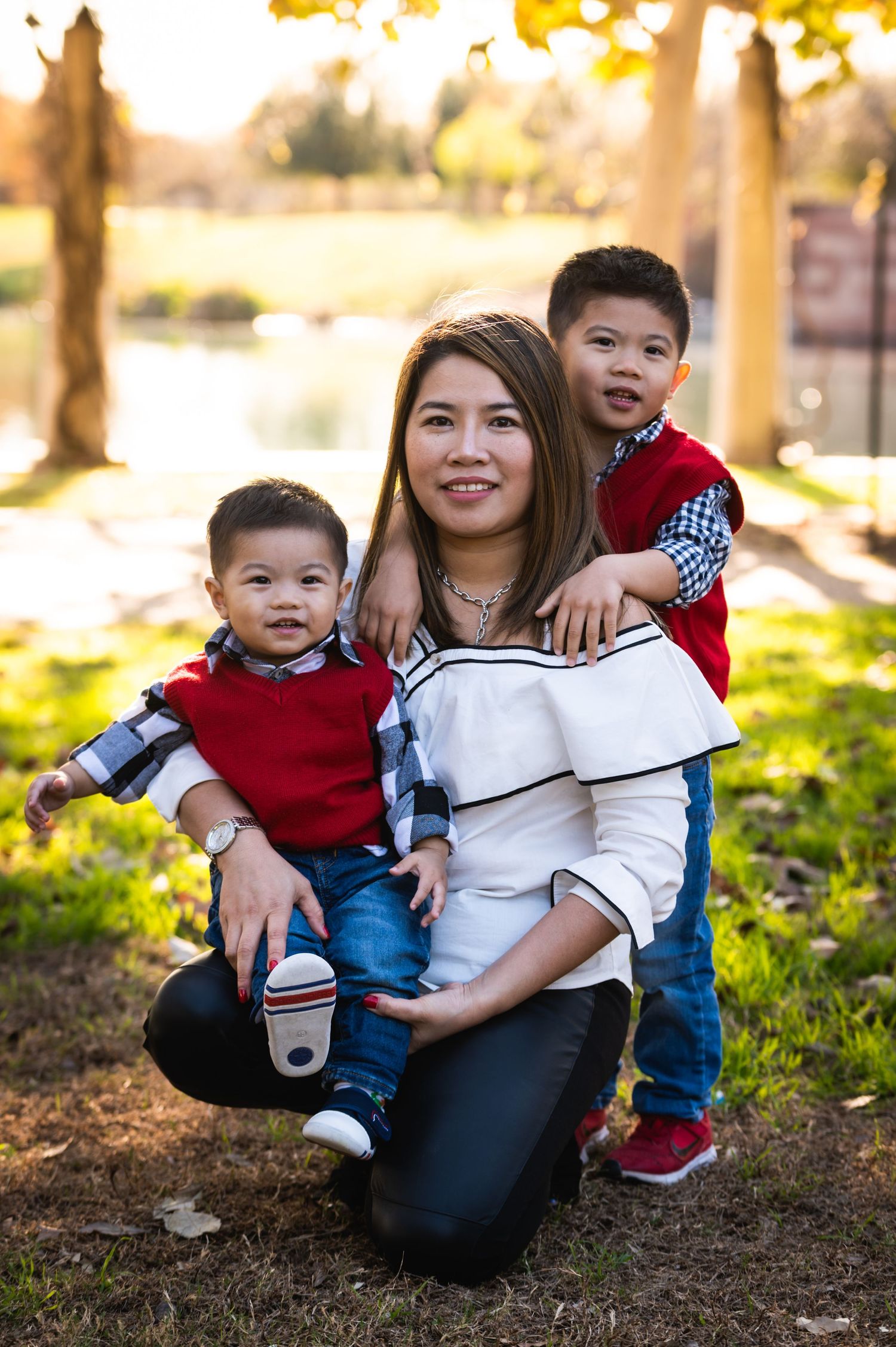 A parent and two small children pose together outdoors during sunset in coordinated outfits.