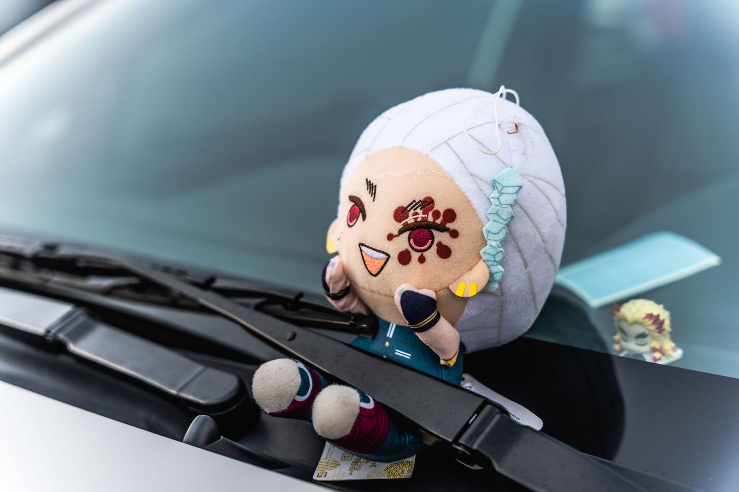 Cute anime character plush toy displayed on a car's dashboard near windshield wipers.