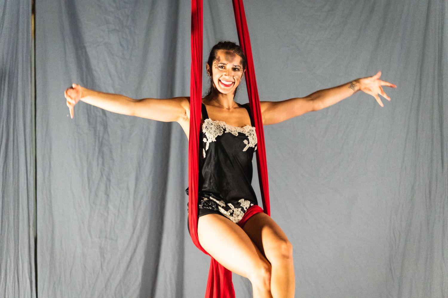 Performer in black costume strikes a pose while suspended on red aerial silks.