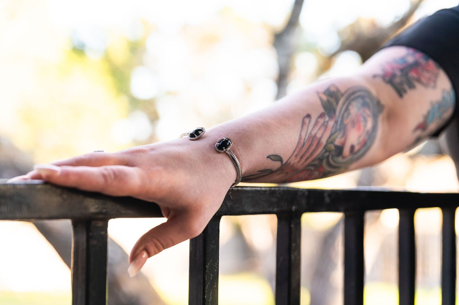 A tattooed arm rests on a railing with small bees inked on the skin.