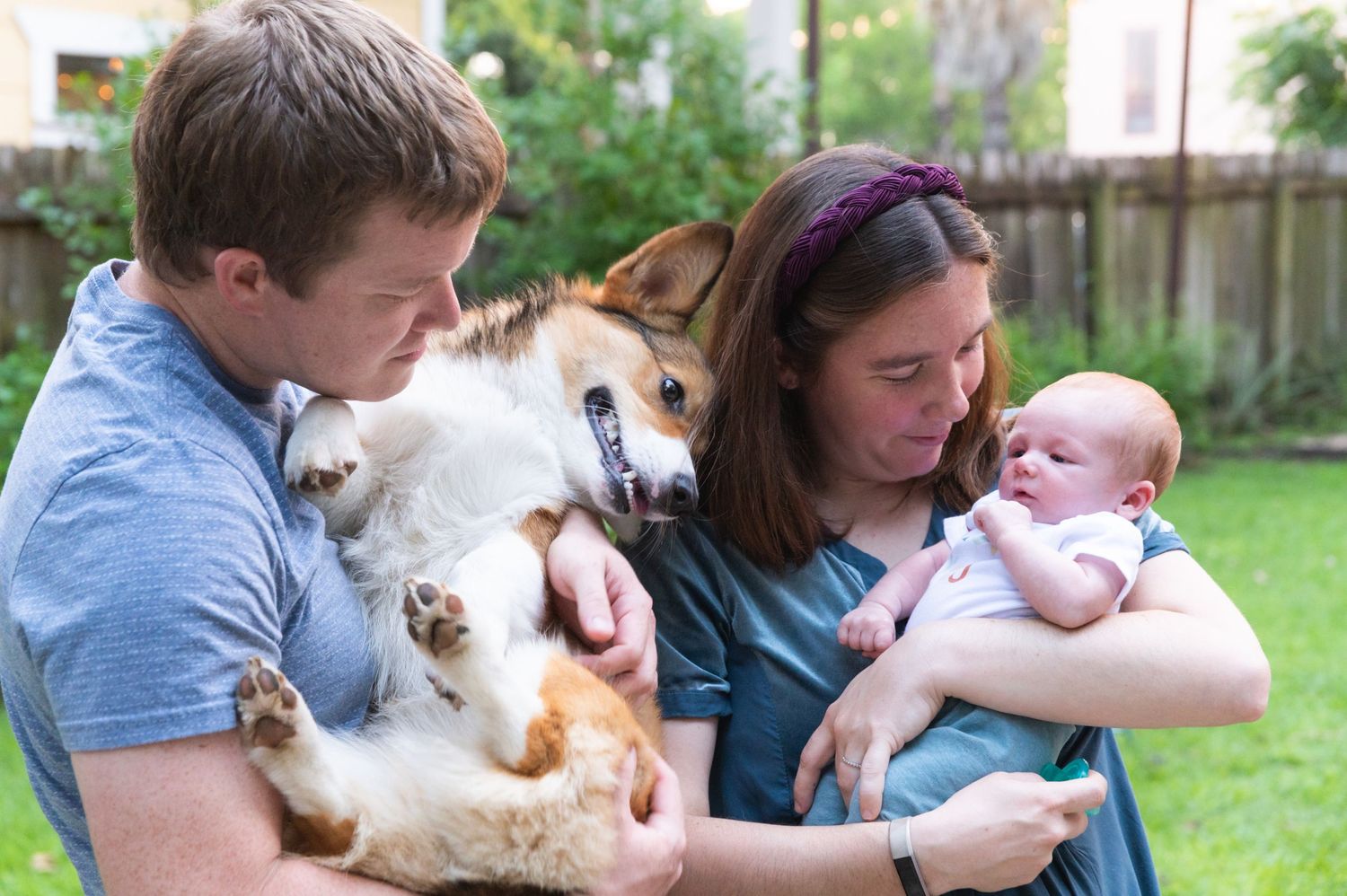 A family moment outdoors with their Corgi pet and young baby in the backyard.