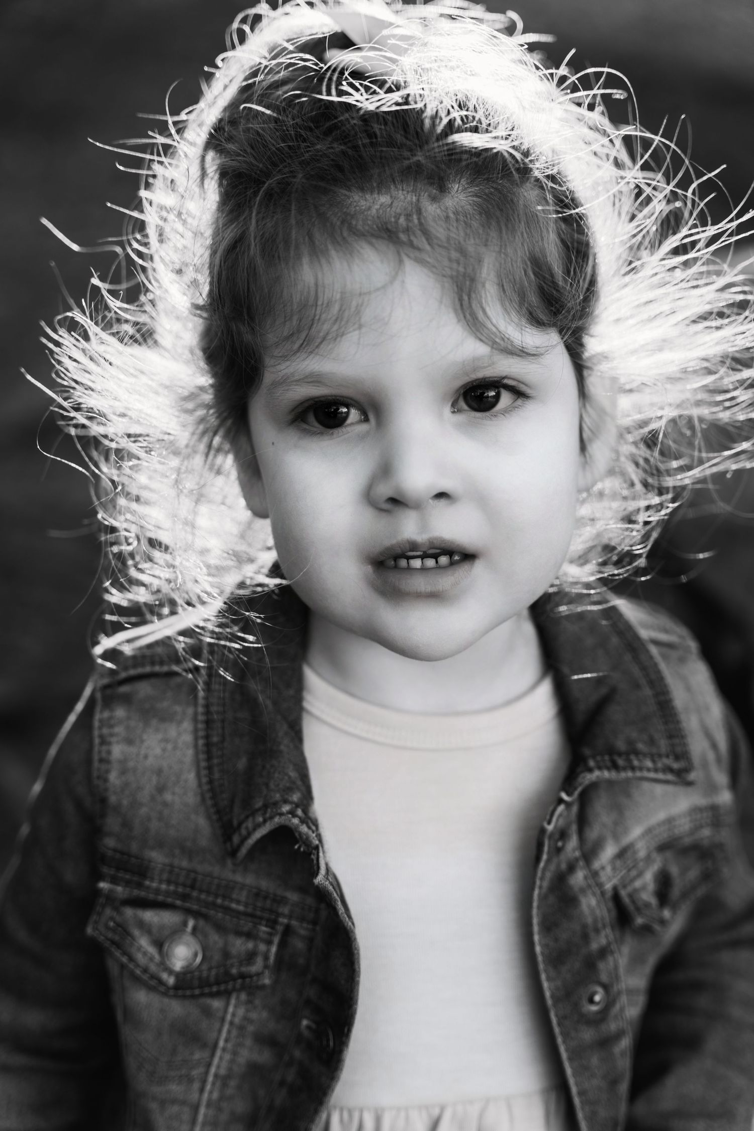Black and white portrait of a small child with windswept hair wearing a denim jacket.