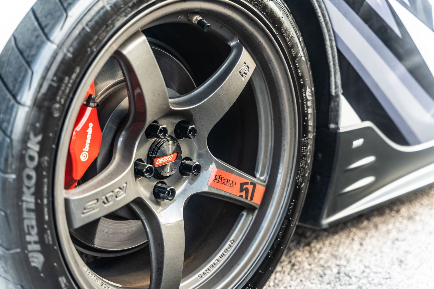 Close-up of a sporty five-spoke wheel with red brake caliper visible behind the gunmetal finished rim.