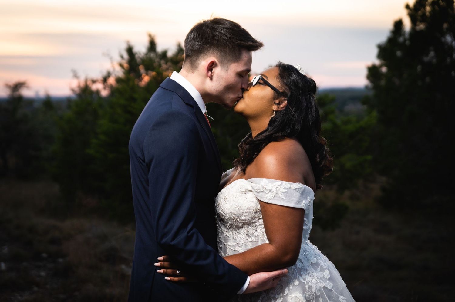 A romantic sunset portrait of newlyweds sharing a kiss against a dusky sky.