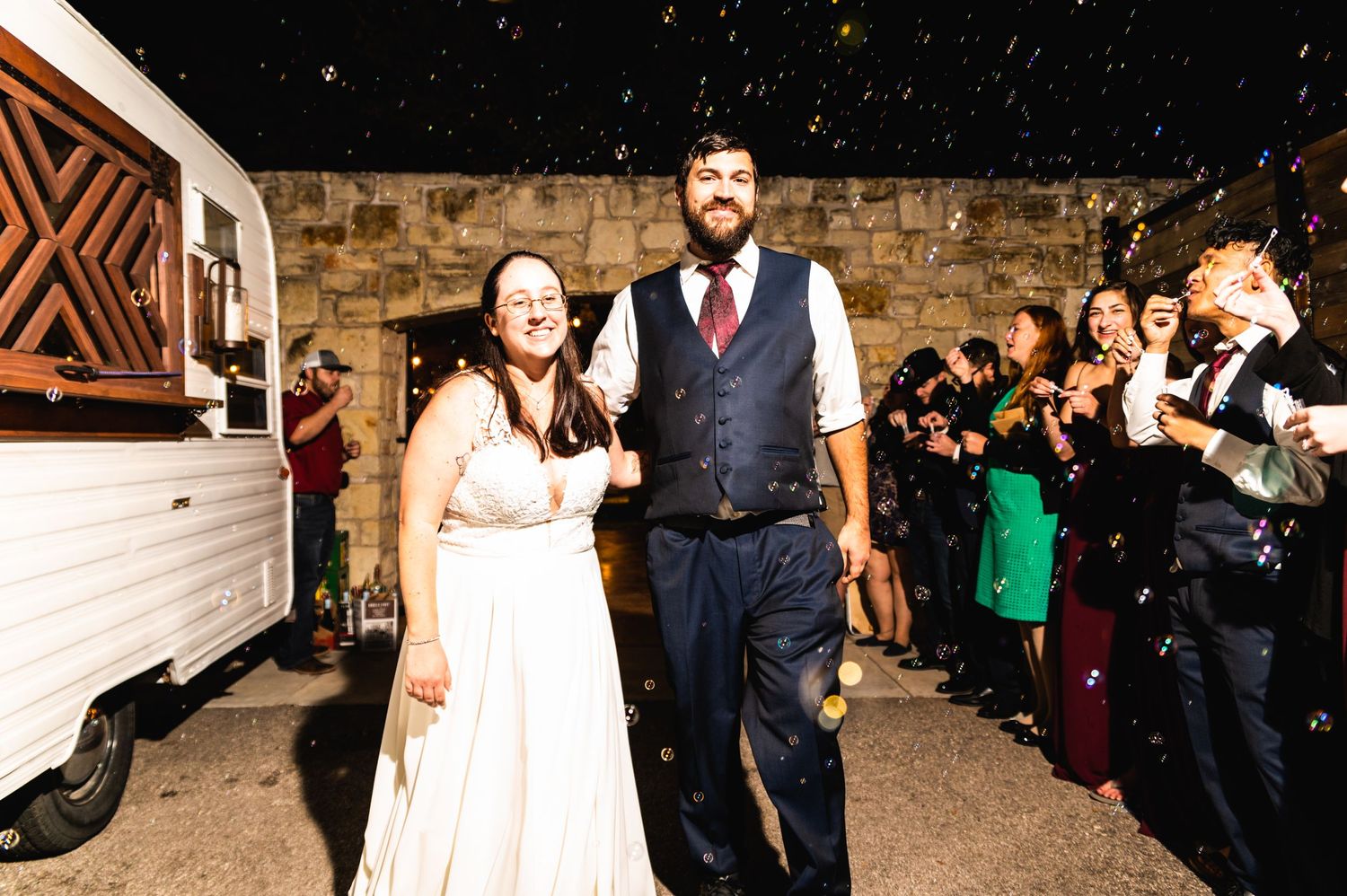 Excited couple walks through sparklers held by wedding guests at night.