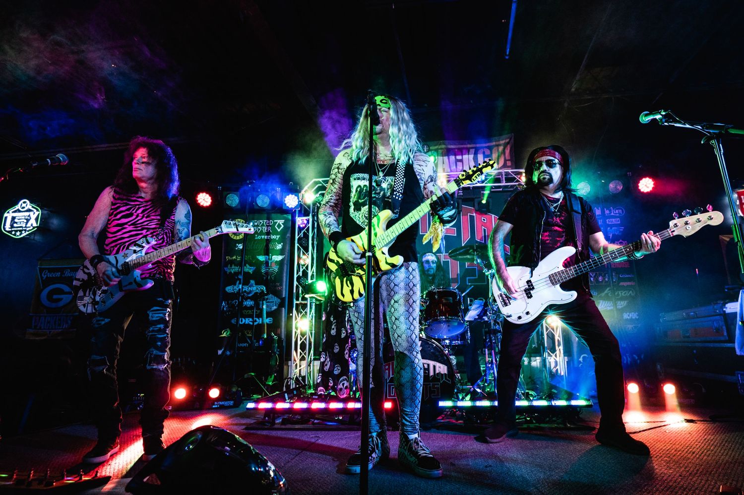 Rock band performing on stage with colorful purple and blue lighting effects.