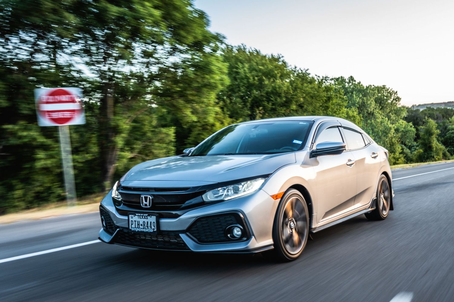 Silver Honda Civic Sport hatchback in motion on a tree-lined road.