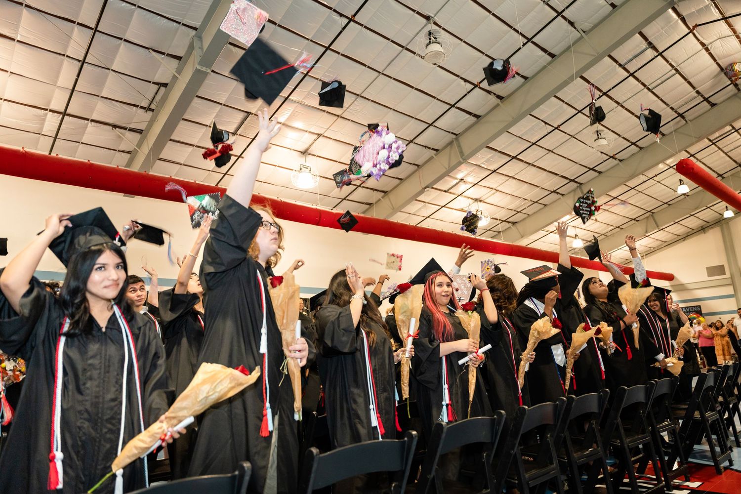 Graduates in black caps and gowns throw their mortarboards in celebration during commencement ceremony.