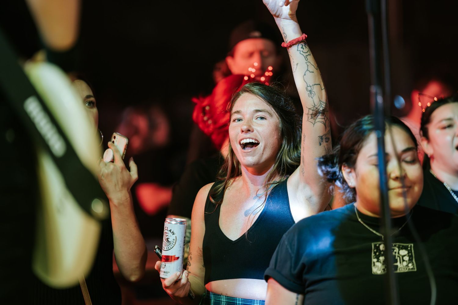 Energetic concert crowd with arms raised enjoying live music in a dimly lit venue.
