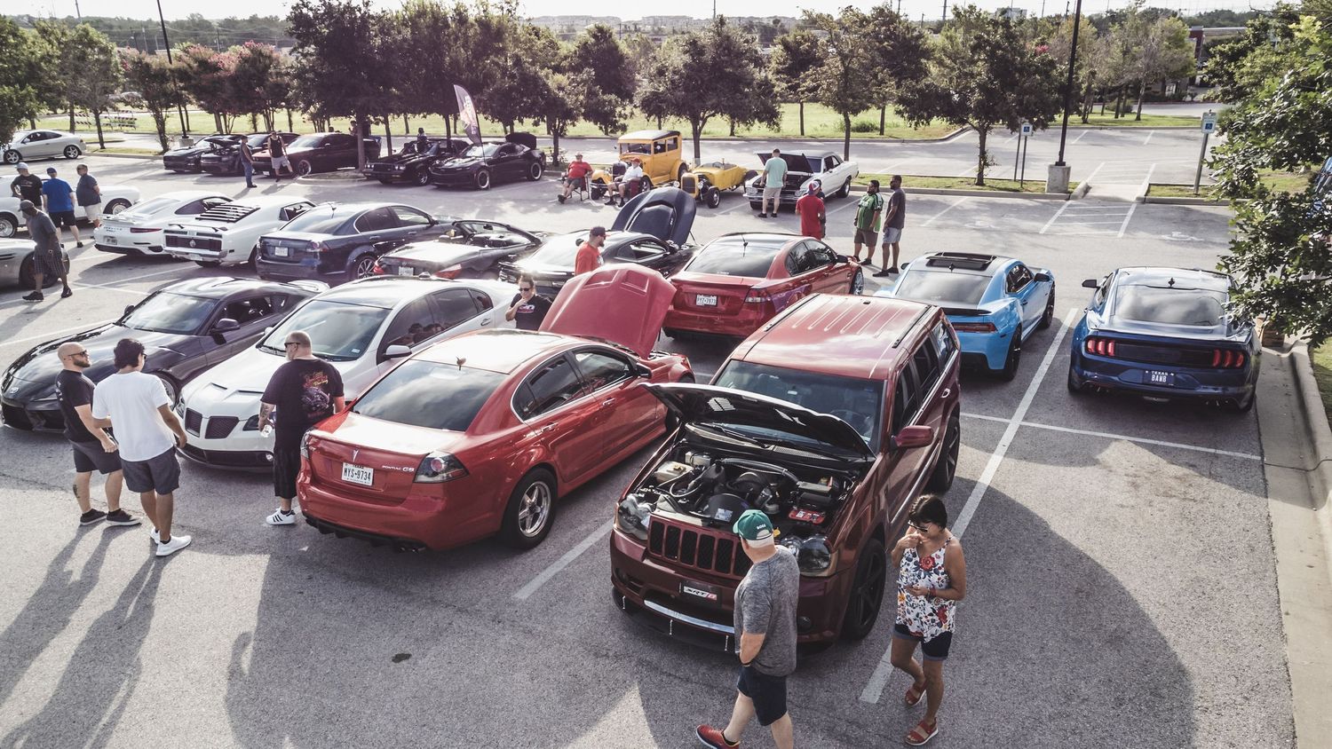 Aerial view of a car meet showing various vehicles parked in rows with attendees gathering.