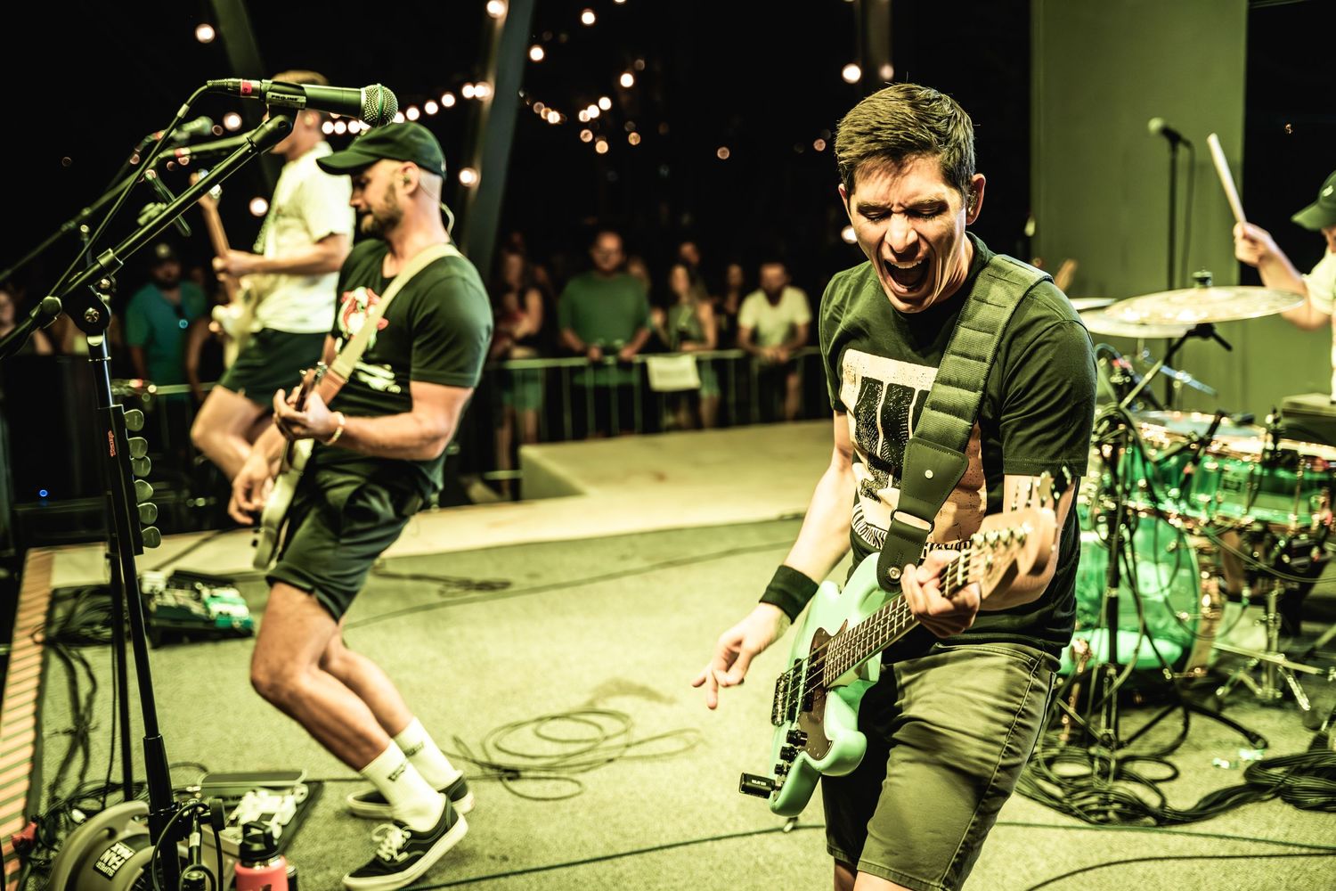 Musicians perform energetically on stage with guitars during a live concert under dramatic lighting.