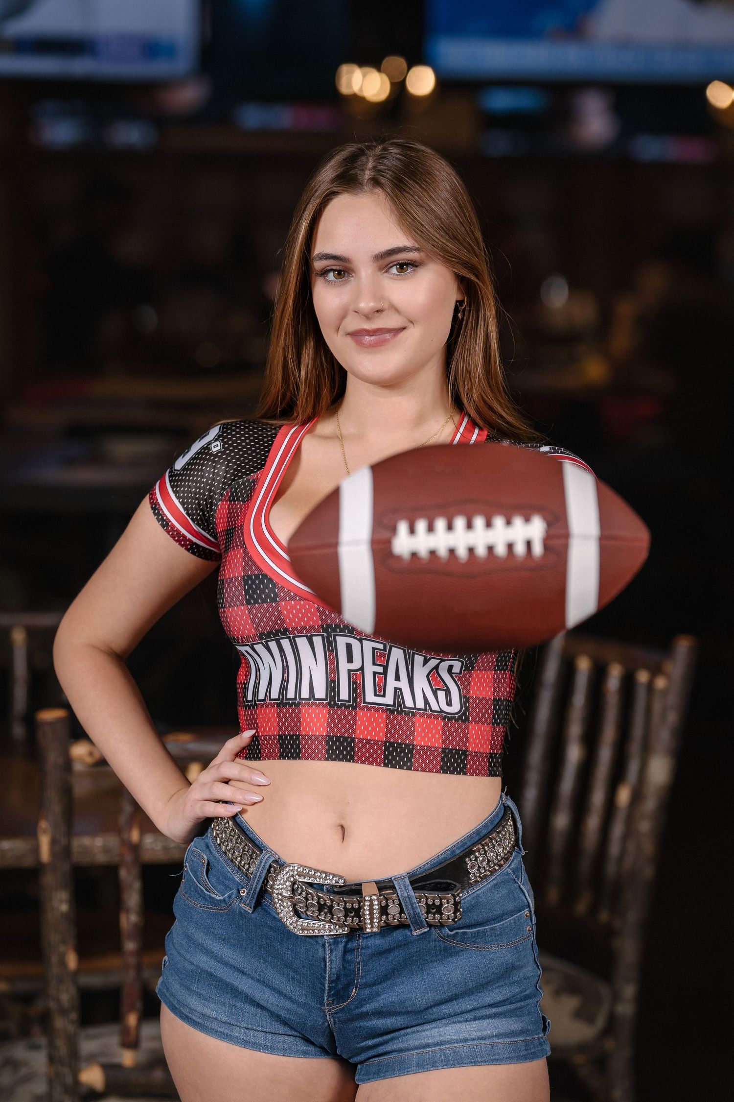 Sports bar promotional shot with football and Twin Peaks branded plaid crop top.